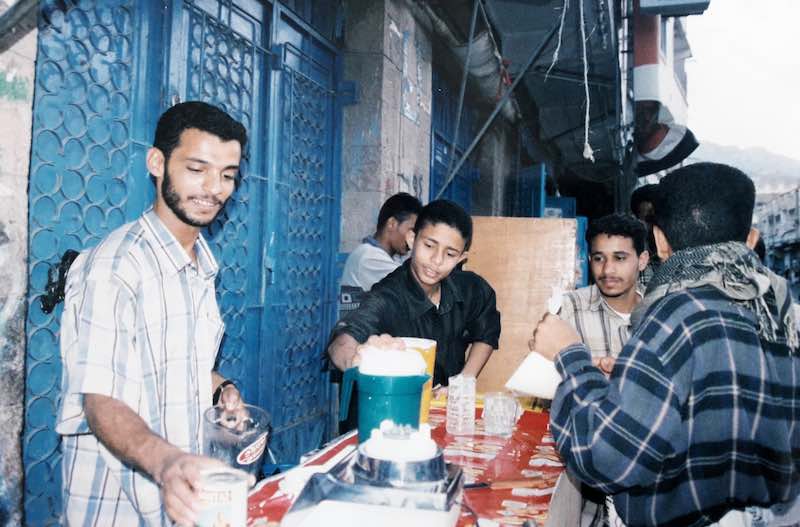 Yazid, Mustafa et Wa'il vendent des sambossas sur un comptoir improvisé, devant le volet fermé d'un magasin.